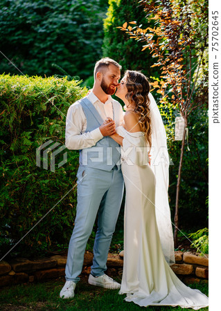 Happy and beautiful bride and groom gently cuddle in the park 75702645