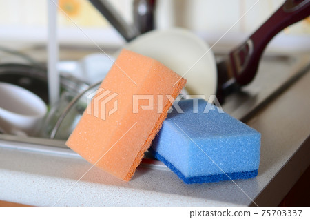 A few sponges lie on the background of the sink with dirty dishes 75703337