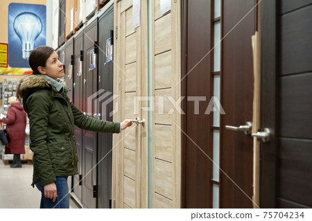 Buyer chooses door in store. Shop window of doors. A large selection of doors for house Buyer chooses door in store. Shop window of doors. A large selection of doors for house 75704234