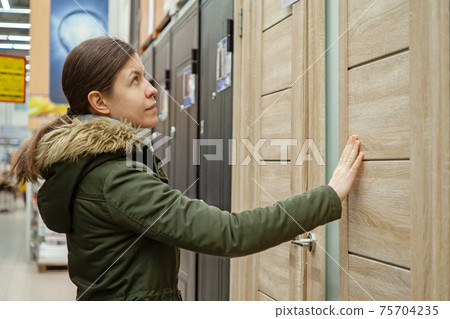 Buyer chooses door in store. Shop window of doors. A large selection of doors for house Buyer chooses door in store. Shop window of doors. A large selection of doors for house 75704235