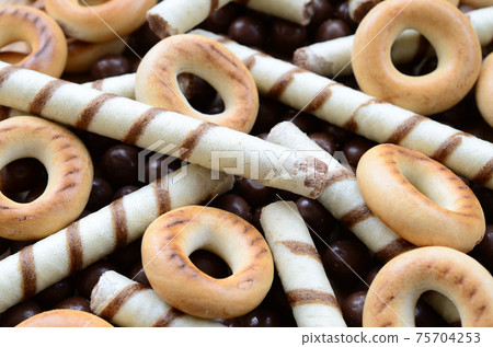 A lot of crispy sweet tubules, chocolate melting balls and yellow bagels lie on a wooden surface. Close up view A lot of crispy sweet tubules, chocolate melting balls and yellow bagels lie on a wooden surface. Close up view 75704253
