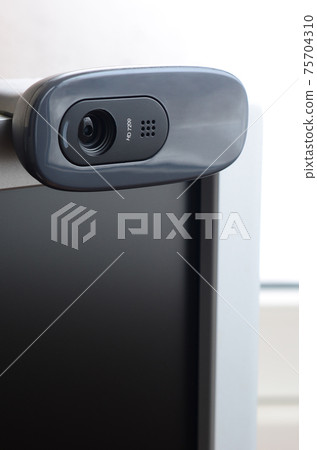 A modern web camera is installed on the body of a flat screen monitor. Device for video communication and recording of high quality video 75704310