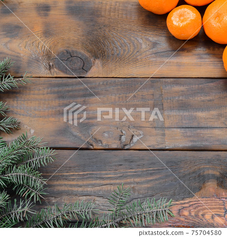 A lot of orange mandarins and Christmas fir branches are lying on a brown wooden planks A lot of orange mandarins and Christmas fir branches are lying on a brown wooden planks 75704580