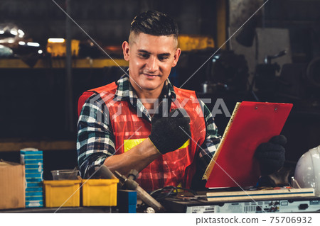 Factory worker talking on portable radio while inspecting machinery parts Factory worker talking on portable radio while inspecting machinery parts 75706932