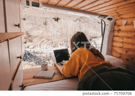 Vanlife - Young woman working on notebook in camping van surrounded by nature 75709706