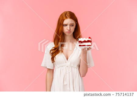 Sad, uneasy and depressed cute redhead girl feeling lonely or heartbroken, eating not to think bad thoughts, holding peace cake and looking distressed at dessert, sighing upset 75714137