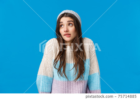 Silly and cute awkward young woman acting uninvolved, biting lip shrugging look away embarrassed, say oops, made mistake avoid eye contact, standing blue background apologizing 75714885