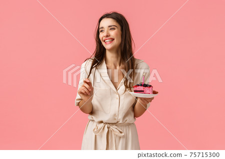 Celebration, happiness and holidays concept. Beautiful young woman having fun, holding plate with cake, smiling and laughing carefree, eating b-day dessert blowing-out candle, having fun 75715300