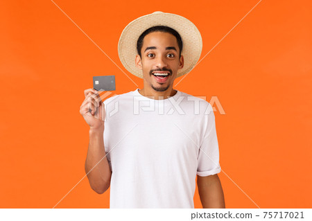 Cute and excited african-american man bought trip vacation for holidays with credit money, holding card and smiling amused, being premium client bank sitting vip terminal airport, orange background 75717021
