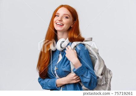 College life, modern lifestyle and education concept. Cheerful good-looking redhead female student with foxy long hair, wearing headphones over neck, backpack, smiling camera 75719261