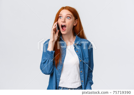 Girl hears amazing great news on phone. Excited lucky redhead girl pick-up phone realises she won challenge, gasping amazed and astonished, holding smartphone near ear, popping eyes surprised 75719390