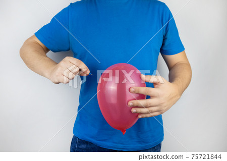 Conceptual photography. The man holds a red ball near his belly, which symbolizes bloating and flatulence. Then he brings a needle to it to burst the balloon and thus get rid of the problem. 75721844