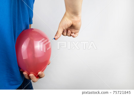 Conceptual photography. The man holds a red ball near his belly, which symbolizes bloating and flatulence. Then he brings a needle to it to burst the balloon and thus get rid of the problem. 75721845
