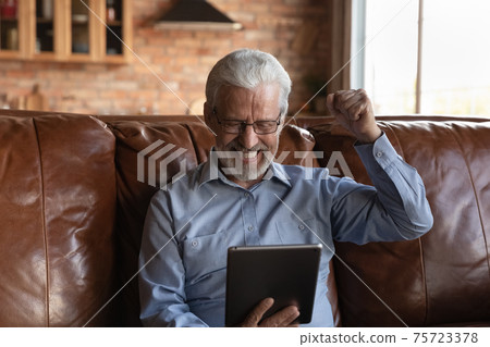 Excited senior man celebrate online win on tablet 75723378