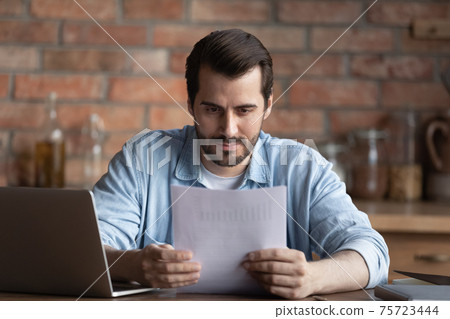 Serious man work on computer reading paperwork Serious man work on computer reading paperwork 75723444