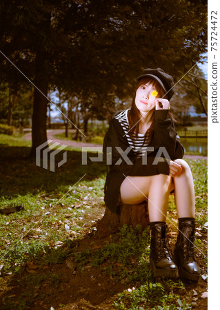 A cute girl sitting on a stump and finding a dandelion during a break 75724472