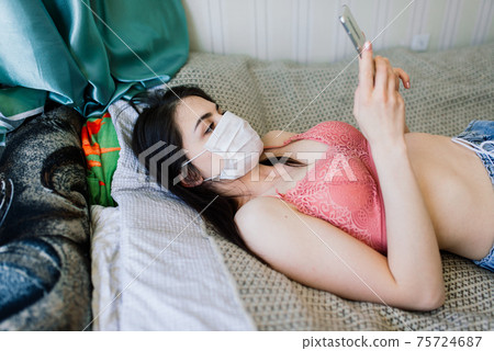 Beautiful female in quarantine wearing protective mask and working at home 75724687