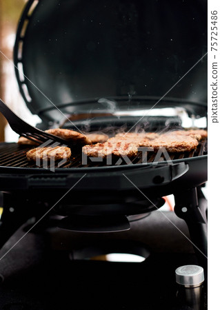 Man grilling steaks on a portable BBQ, Snowy winter barbecue Man grilling steaks on a portable BBQ, Snowy winter barbecue 75725486
