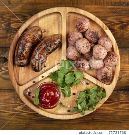 Fried sausages and meat balls with sauce and herbs on a wooden plate. Top. Fried sausages and meat balls with sauce and herbs on a wooden plate. Top. 75725768
