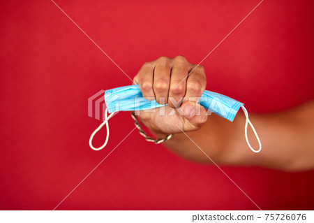 Men Hand holding a protection medical mask on red studio background Men Hand holding a protection medical mask on red studio background 75726076