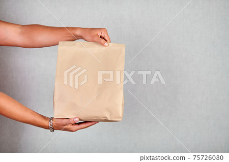 Closeup courier hand holding grocery paper bag, delivery service Closeup courier hand holding grocery paper bag, delivery service 75726080