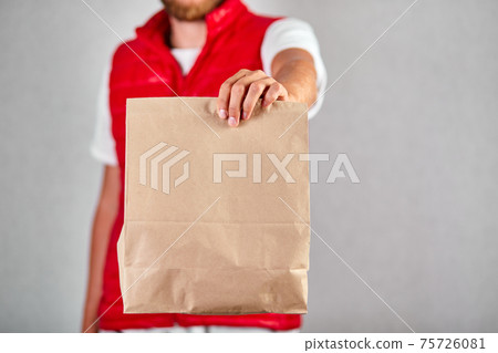 Courier, delivery man in red vest uniform delivers online purchases in brown paper bags Courier, delivery man in red vest uniform delivers online purchases in brown paper bags 75726081