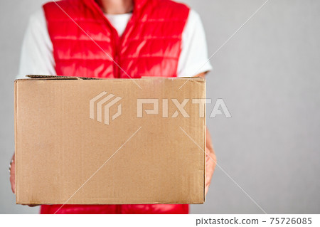 Delivery man employee in red vest uniform hold empty cardboard box Delivery man employee in red vest uniform hold empty cardboard box 75726085