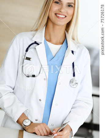 Woman-doctor at work in clinic happy of her profession. Blond female physician controls medication history record and medical exam results. Medicine concept 75726178