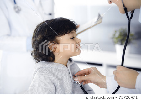 Woman-doctor examining a child patient by stethoscope. Cute arab toddler at physician appointment. Medicine concept Woman-doctor examining a child patient by stethoscope. Cute arab toddler at physician appointment. Medicine concept 75726471