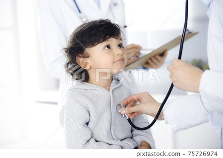 Woman-doctor examining a child patient by stethoscope. Cute arab toddler at physician appointment. Medicine concept Woman-doctor examining a child patient by stethoscope. Cute arab toddler at physician appointment. Medicine concept 75726974