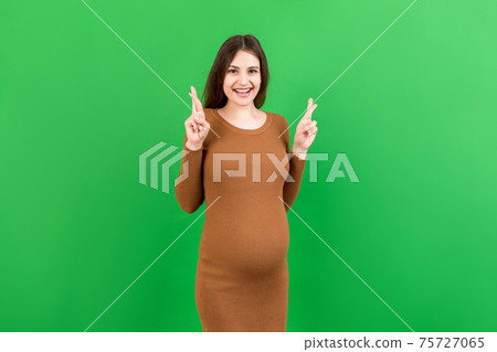 Cheerful young pregnant woman holding fingers crossed, waiting pregnancy isolated on colored background in studio. lifestyle pregnancy concept 75727065
