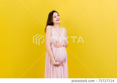 Happy pregnant woman touching her abdomen at Colored background. Future mother is wearing white underwear. Expecting of a baby. Copy space Happy pregnant woman touching her abdomen at Colored background. Future mother is wearing white underwear. Expecting of a baby. Copy space 75727114