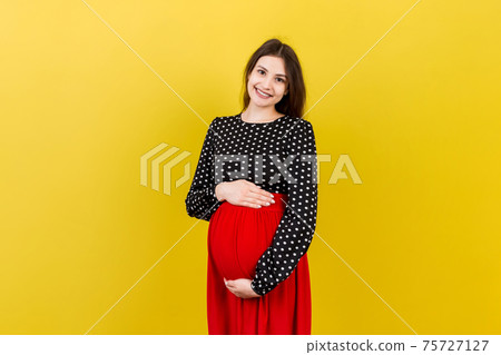 Happy pregnant woman touching her abdomen at Colored background. Future mother is wearing white underwear. Expecting of a baby. Copy space Happy pregnant woman touching her abdomen at Colored background. Future mother is wearing white underwear. Expecting of a baby. Copy space 75727127