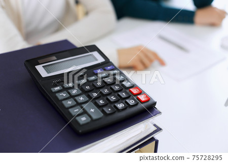 Calculator and binders with papers are waiting to be processed by business woman or bookkeeper working at the desk in office back in blur. Internal Audit and tax concept 75728295