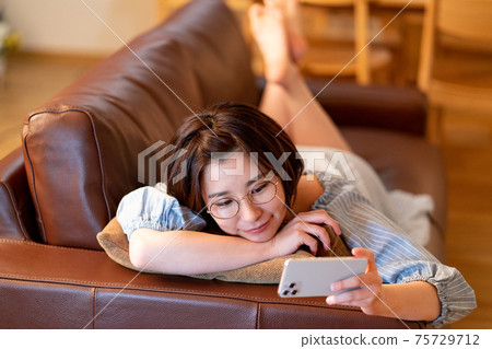 一個年輕的女人，晚上在客廳裡看她的智能手機上的視頻 75729712