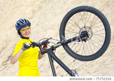 beautiful woman cyclist with bike against the background of the Sands.  beautiful woman cyclist with bike against the background of the Sands.  75732520