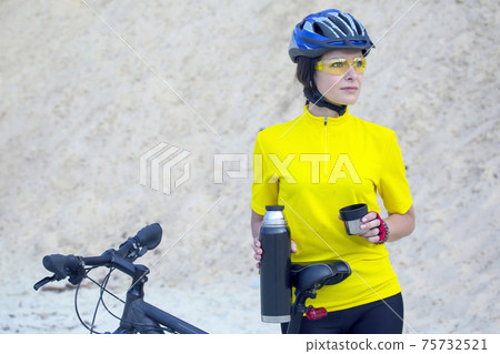 Beautiful girl cyclist in yellow with tea and thermos in hand 75732521