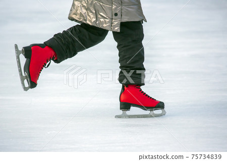 feet in red skates on an ice rink. Hobbies and sports. Vacations and winter activities. 75734839