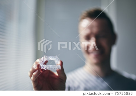 Smiling young man holding trays for teeth whitening 75735883