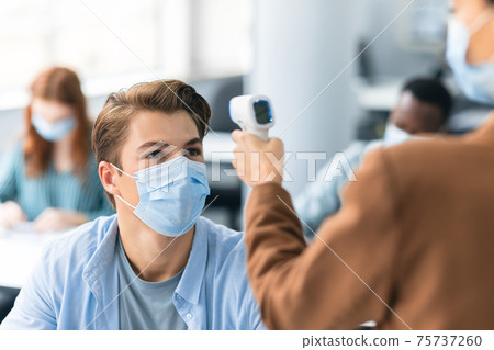 Teacher with contactless thermometer gun measuring temperature of male student 75737260