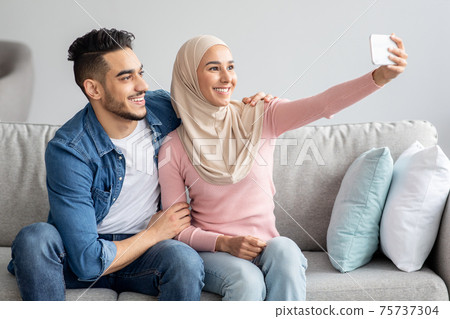 Handsome man and woman in hijab smiling at smartphone camera 75737304