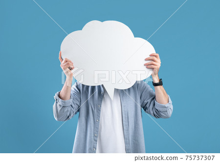 Faceless young man covering his face with speech bubble on blue studio background, mockup for design Faceless young man covering his face with speech bubble on blue studio background, mockup for design 75737307