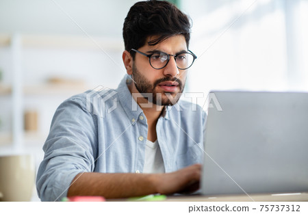 Concentrated arabic male freelancer working on laptop at home office, typing on computer keyboard 75737312