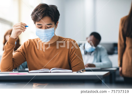 Male asian student in mask sitting at desk in class 75737319