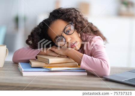 Sleepy african-american teen girl resting head on paper books, tired of school, studying and reading Sleepy african-american teen girl resting head on paper books, tired of school, studying and reading 75737323