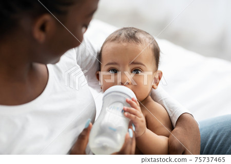 Cute little African American baby drinking from baby bottle Cute little African American baby drinking from baby bottle 75737465