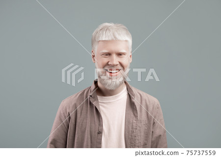 Happy albino man with white skin and hair posing with confident smile on grey studio background Happy albino man with white skin and hair posing with confident smile on grey studio background 75737559