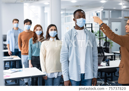 Woman with gun thermometer cheking diverse people temperature in line Woman with gun thermometer cheking diverse people temperature in line 75737820