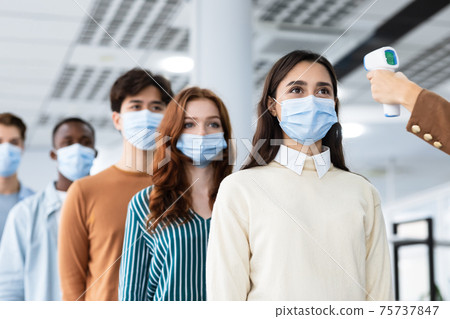Woman with contactless thermometer cheking multiracial people temperature in queue Woman with contactless thermometer cheking multiracial people temperature in queue 75737847