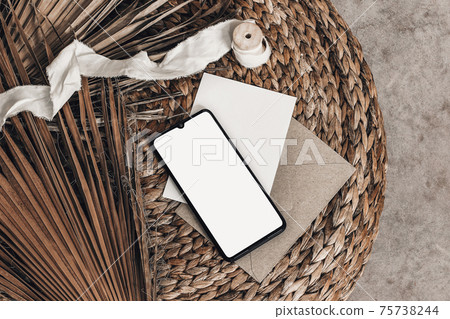 Tropical summer mockups. Black cell phone with empty screen, blank greeting card, envelope and ribbon placed on rattan straw pouff. Dry palm leaves. Minimal modern boho interior, flat lay, top view. Tropical summer mockups. Black cell phone with empty screen, blank greeting card, envelope and ribbon placed on rattan straw pouff. Dry palm leaves. Minimal modern boho interior, flat lay, top view. 75738244